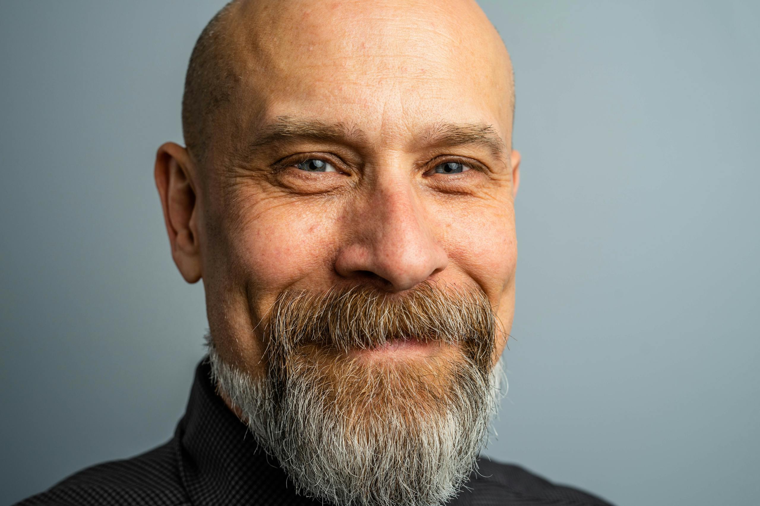 Close-up portrait of a mature bald man with a full beard, exuding confidence and style in a professional studio setting.